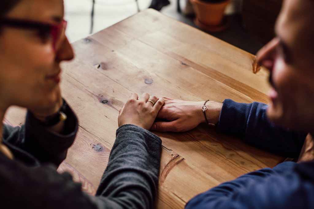 Couple sitting at a table, holding hands.