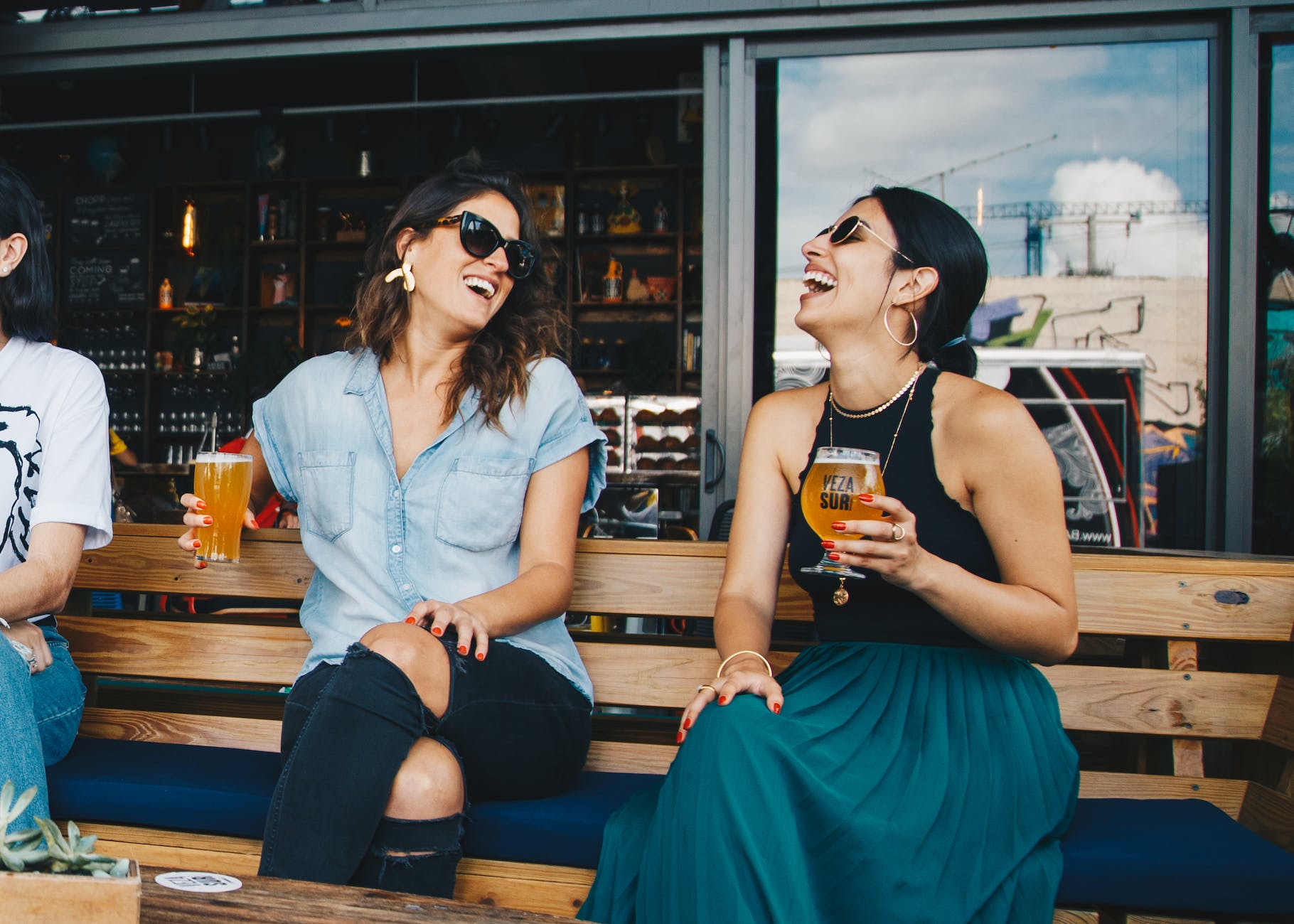 Friends drinking beer sitting in a bench.