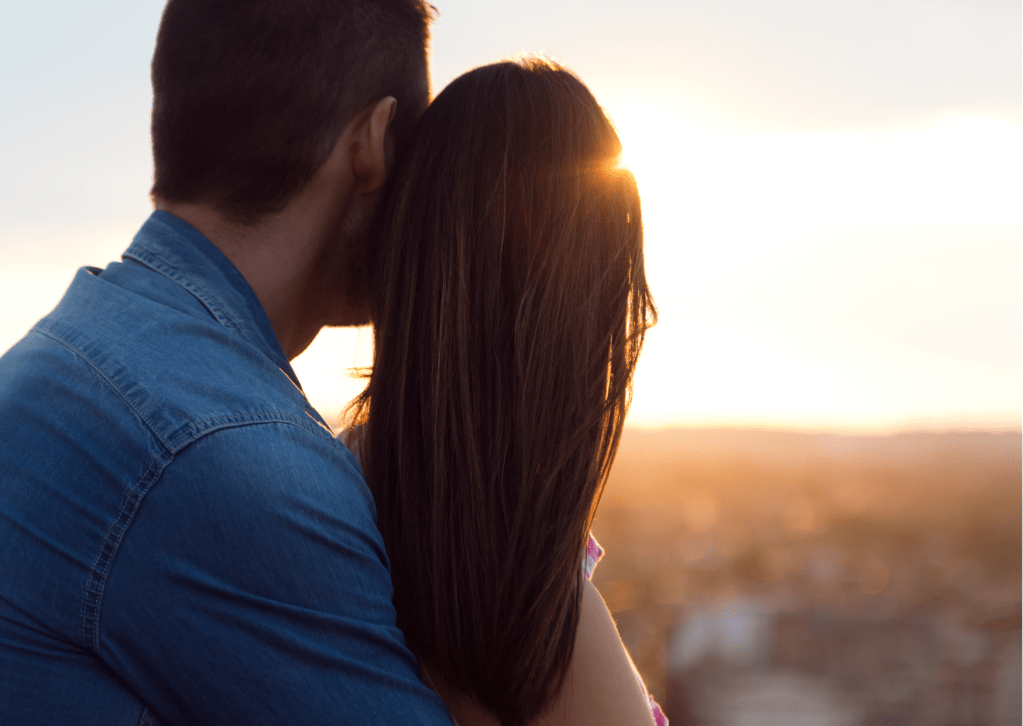 Young couple embrace on a roof looking at sunset